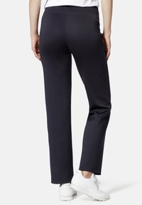 Schwarze Sporthose mit gerader Schnittführung, elastischem Bund und glatter Textur, kombiniert mit weißen Sneakers.