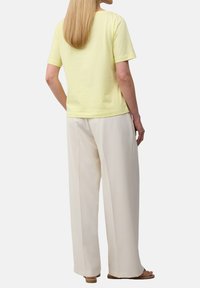 Żółta bawełniana koszulka z krótkim rękawem, zestawiona z kremowymi spodniami o szerokich nogawkach. Gładka tekstura, minimalistyczny design i luźny krój.