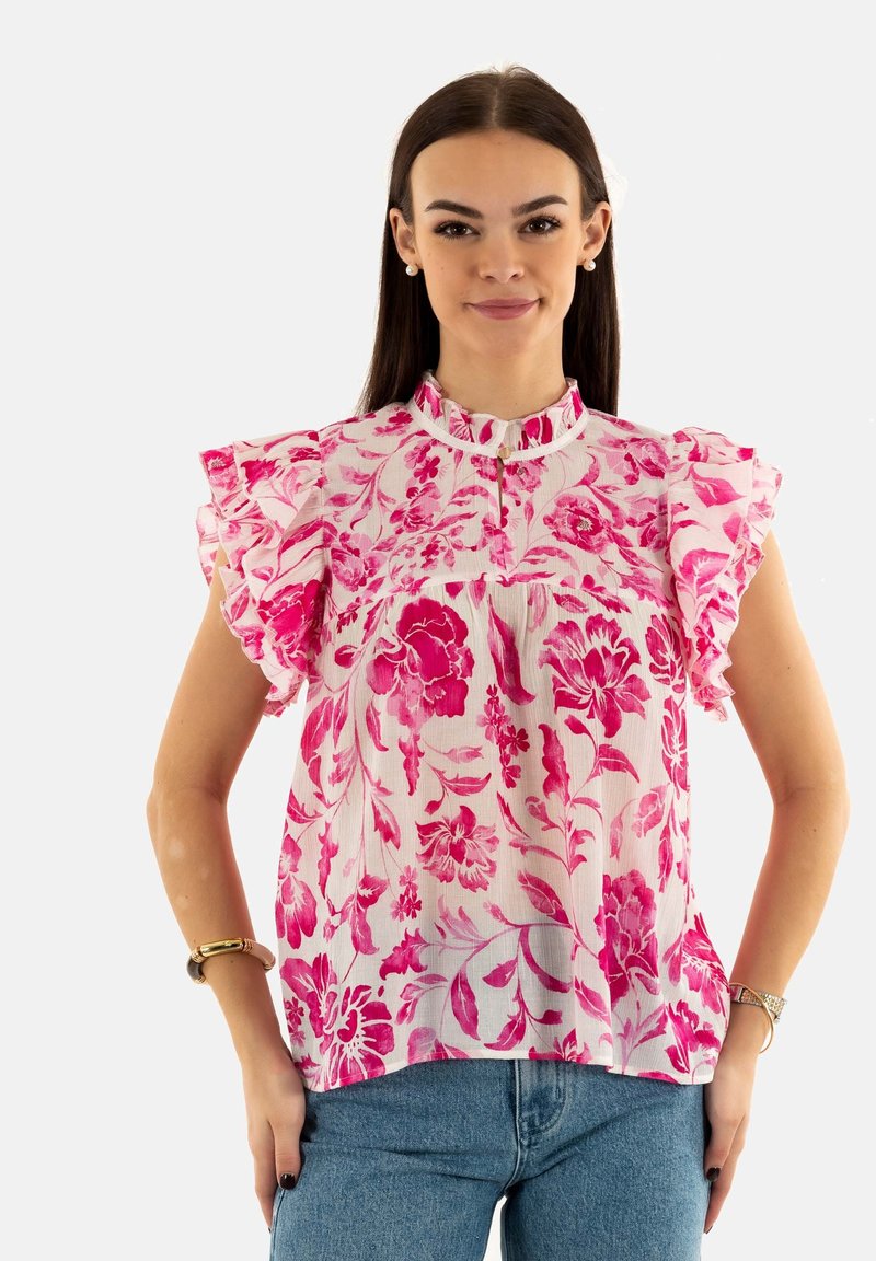 Blusa floral rosa con mangas acampanadas, con cuello alto y patrón floral vertical en tejido ligero. Combinada con jeans azules.