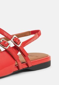 Red patent leather sandal with multiple narrow straps and silver buckles, featuring a flat black sole and a textured footbed.