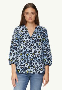 Lekka, niebieska bluzka z wzorem w panterkę w kolorze czarnym i żółtym. Posiada dekolt w kształcie litery V oraz rękawy o długości trzy czwarte z bufkami.