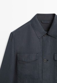 Chemise boutonnée gris foncé avec col pointu et deux poches plaquées poitrine à rabats, vue de face et cadrée aux épaules.