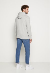 Grijze hoodie met een comfortabele pasvorm, geribbelde manchetten en zoom, gecombineerd met lichtblauwe spijkerbroeken en witte sneakers. Effen achtergrond.