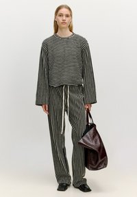 Zwart-wit gestreepte cropped trui en bijpassende broek met een trekkoord in de taille. Het model houdt een glanzende bordeaux kleurige tote bag vast.