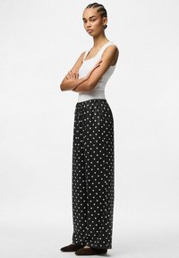 Melni punktiņi bikses ar brīvu piegriezumu, gumijas josta un plašiem, platām kājām, apvienotas ar baltu pieguļošu topu. Dzeltenas plakanas kurpes.