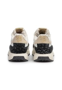 Pari valkoisia ja mustia lenkkareita, joissa on beige korko, kultainen logo ja pörröinen vuori, nähtynä takaa valkoista taustaa vasten.