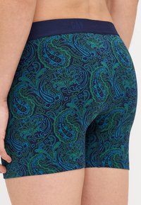 Námorné boxerky s paisley vzorom v modrých a zelených odtieňoch, s pevným pásom označeným "GAP" v oblasti pása. Mäkká, pružná tkanina.
