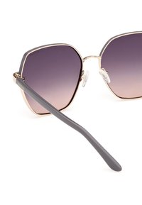 Sluneční brýle s velkými čtvercovými čočkami, které přecházejí od tmavě fialové k světle fialové. Zlaté kovové akcenty a šedé plastové bočnice s průhlednými nosními podložkami.