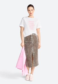 Witte T-shirt met roze tekst, middelgrote rok met luipaardprint, en een lichtroze hoodie die over de arm hangt. Lichtroze sneakers.