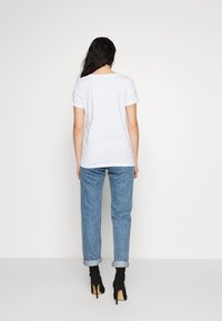 White short-sleeve t-shirt, relaxed fit, paired with light blue rolled-up denim jeans and black heeled ankle boots, shown from the back.