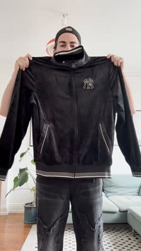 Svart zip-up jakke med myk tekstur, hvite stripe detaljer på ermene og kanten, samt en logo på brystet. Den har sidelommer.