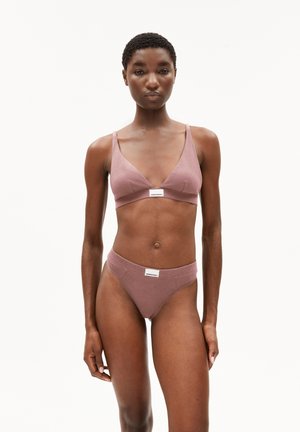 Woman with short curly hair wearing dusty pink bralette and matching high-cut briefs against a plain white background.