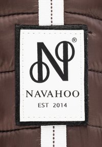 Brown fabric label featuring the logo "N" with circular accents, and the brand name "NAVAHOO" above "EST 2014," bordered by a black frame.