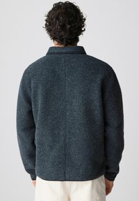 Giacca di lana grigia scura con colletto, spalle basse e maniche lunghe. Dettagli delle cuciture sul retro e vestibilità rilassata.