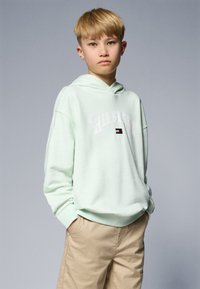 Svetlo mint zelena kapuca z sprednjim žepom in belim logotipom "HILFIGER". Ujemite z bež kratkimi hlačami. Mehka tekstura in sproščen kroj.
