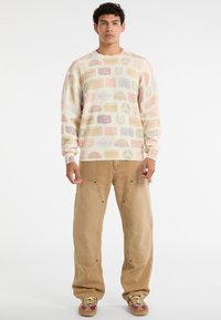 Sweatshirt met een crèmekleurige achtergrond en meerkleurige grafische patronen, met geribbelde manchetten en een relaxte pasvorm. Gecombineerd met tan cargo broeken.