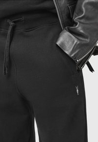 Pantalones de chándal negros hechos de un tejido suave, con una cintura ajustable con cordón y bolsillos laterales. Pequeño detalle bordado cerca del bolsillo.