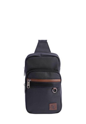 Bolso de lona negro con acento de cremallera marrón, un compartimento principal y un bolsillo frontal, con un parche de logo y una correa ajustable.