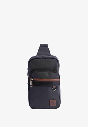 Bolso de lona negro con acento de cremallera marrón, un compartimento principal y un bolsillo frontal, con un parche de logo y una correa ajustable.