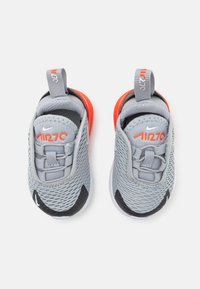 Baskets en maille grises avec des accents rouges, semelle noire et lacets gris. Comprend une languette pour un enfilage facile et le logo Nike sur le côté.