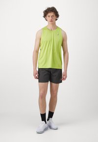 Limegrøn ærmeløs sports-top, sorte shorts, hvide sneakers og sorte ankelstrømper. Glat stof, afslappet pasform og logodetalje.