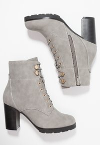 Bottines grises en daim avec talons noirs épais, lacets avant avec œillets dorés et fermeture éclair latérale sur une botte.