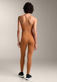 Barna sportmelltartó, keresztpántokkal, amelyet összeillő, magas derekú leggings-szel párosítottak, mindkettő sima, rugalmas anyagból készült.