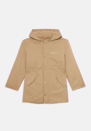 Chaqueta beige con capucha, botones frontales, dos bolsillos y logo "Versace Milano" en el lado izquierdo del pecho.