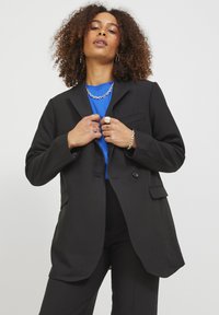 Black blazer with a structured design, featuring two buttons, front pockets, and a smooth texture, worn over a blue top.
