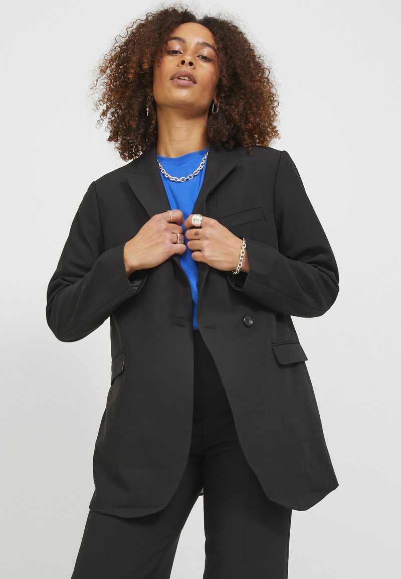 Black blazer with a structured design, featuring two buttons, front pockets, and a smooth texture, worn over a blue top.