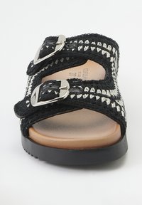 Sandale tissée noir et blanc avec deux boucles réglables à accents métalliques, une semelle intérieure lisse couleur tan et une semelle extérieure texturée noire.