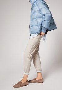 Padded blue jacket with a cropped design, beige rolled-up trousers, and brown suede loafers featuring a strap detail. Striped shirt underneath.