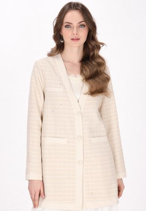 Lysbeige blazer med et struktureret ternet mønster, reverskrave, to frontlommer og dekorative knapper. Blødt stof med subtil glans.