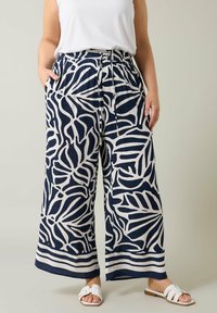 Pantalones de pierna ancha en azul marino y crema con un patrón de hojas, cintura elástica, cierre con cordón y bolsillos laterales. Combinados con una blusa blanca y sandalias.