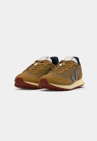 Sneakers in rete e suede marroni con suola crema, accenti grigi e lacci marroni, dotati di colletto imbottito e suola testurizzata.