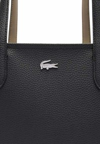 Sac fourre-tout en cuir noir avec une finition texturée, ornée d'un accent en logo crocodile argenté à l'avant. Poignées robustes pour le transport.