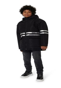 Veste noire DKNY avec capuche, rayures argentées réfléchissantes et grandes poches avant. Associée à un jean foncé et des baskets noires.
