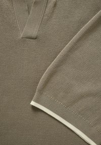 Pull marron tricoté avec col en V et manches longues, orné d'une bordure blanche au niveau du poignet.