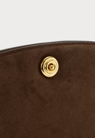 Κοντινή λήψη από μια καφέ σουέτ επιφάνεια με ένα στρογγυλό, λαμπερό χρυσό κουμπί στο κοντινό άκρο.