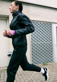 Sort atletisk jakke med høj krave, parret med sorte bukser og sorte løbesko. Har pink ærmekanter og hvide sokker.
