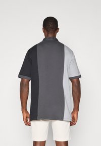 Cămașă polo cu mânecă scurtă, cu un design în blocuri de culoare în negru, gri închis și gri deschis. Material din bumbac moale, cu guler clasic.