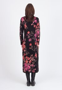 Long black dress with floral pattern in red and pink, long sleeves, fitted bodice, and side slits, paired with knee-high black boots.