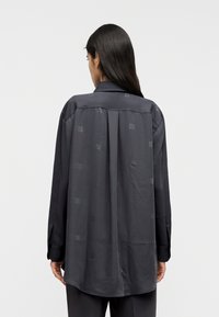 Σκούρο γκρι μ ακρυμάνικο πουκάμισο με διακριτικό μοτίβο με λογότυπα σε όλο το ύφασμα, διαθέτοντας ένα πιέτα στην πλάτη και κλασικό γιακά. Λείο ύφασμα, άνετη εφαρμογή.