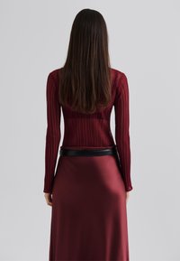 Haut à manches longues bourgogne avec des rayures texturées, associé à une jupe lisse et saténée avec une ceinture noire.