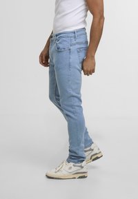 Vaaleansiniset slim fit -farkut, joissa on klassinen viiden taskun muotoilu ja hienovaraiset ompeluyksityiskohdat. Yhdistetty valkoisiin urheilukenkiin.