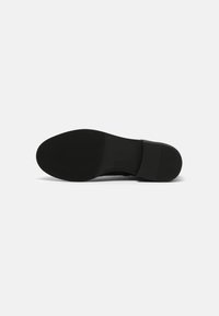 Suela de zapato negra con una textura suave y un ligero patrón de dibujo. Presenta una forma contorneada con un tacón plano y un sutil detalle de marca.