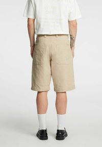 Beige stripete shorts med to baklommer, knelengde og oppbrettet kant. Brukes med hvite sokker og svarte sko, kombinert med en grafisk t-skjorte.