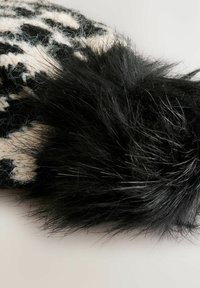Uldtilbehør med et geometrisk mønster i sort og creme, der har en fluffy sort kunstpelskant. Teksturen er blød og tæt.