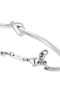 Pulsera de metal de color plateado con un diseño de nudo abierto y un cierre de cadena que incluye una pequeña etiqueta grabada que dice "BREIL."