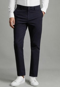 Chino marine en tissu mélangé de coton, avec une taille plate, des poches latérales et une coupe slim, associés à des baskets blanches.